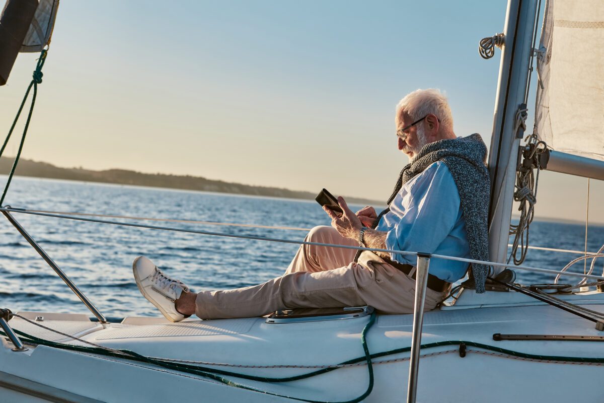 BRAIN Yachting Entschleunigen relax Spending some time alone. Side view of a relaxed senior man sitting on the side of sailboat or yacht deck floating in the sea at sunset